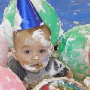 photo of a baby surrounded by balloons and white messy  foam