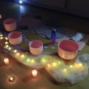 Pink Singing Bowls and Candles lined up next to a yoga mat. 